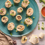 A picture of buffalo chicken pinwheel sandwiches on a plate with buffalo sauce on the side.