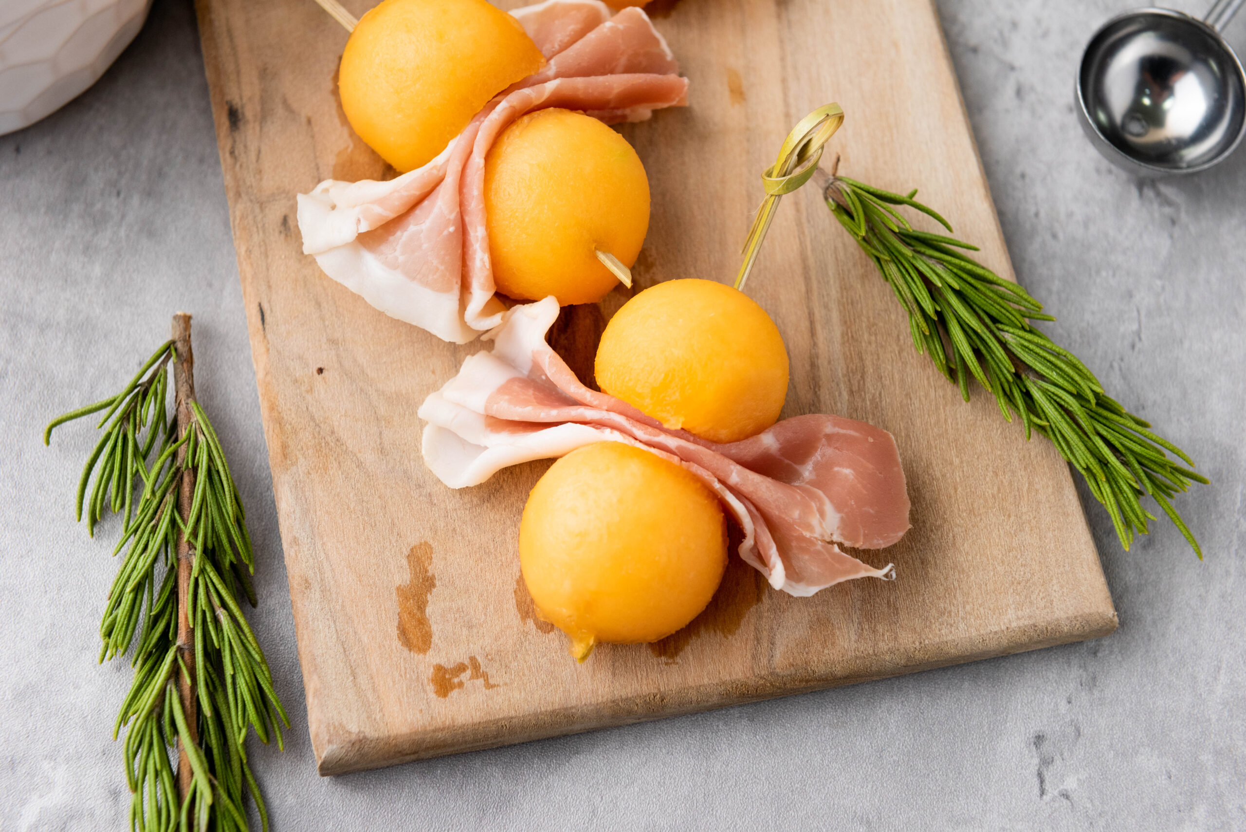 A picture of cantalope prosciutto skewers on a wooden serving platter.