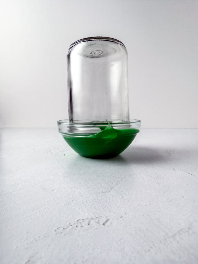 A picture of a jar being dipped in green frosting.