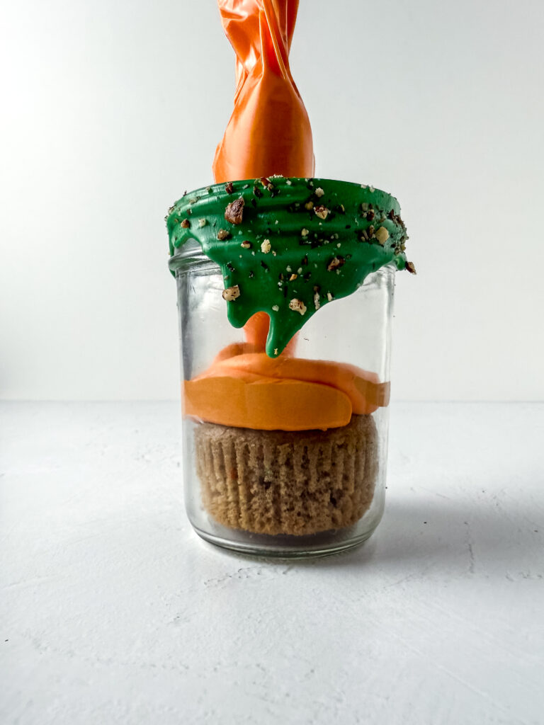 A picture of a carrot cake muffin in a jar with orange frosting on the top.