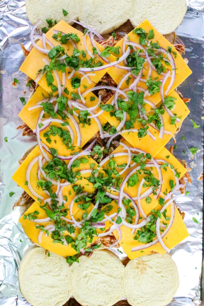 A picture of hawaiian rolls cut in half, topped with barbecue chicken cheese, red onions, and chopped cilantro..