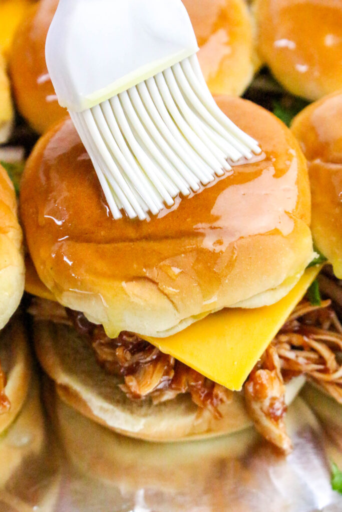 A picture of a chicken slider being brushed over the top with butter.