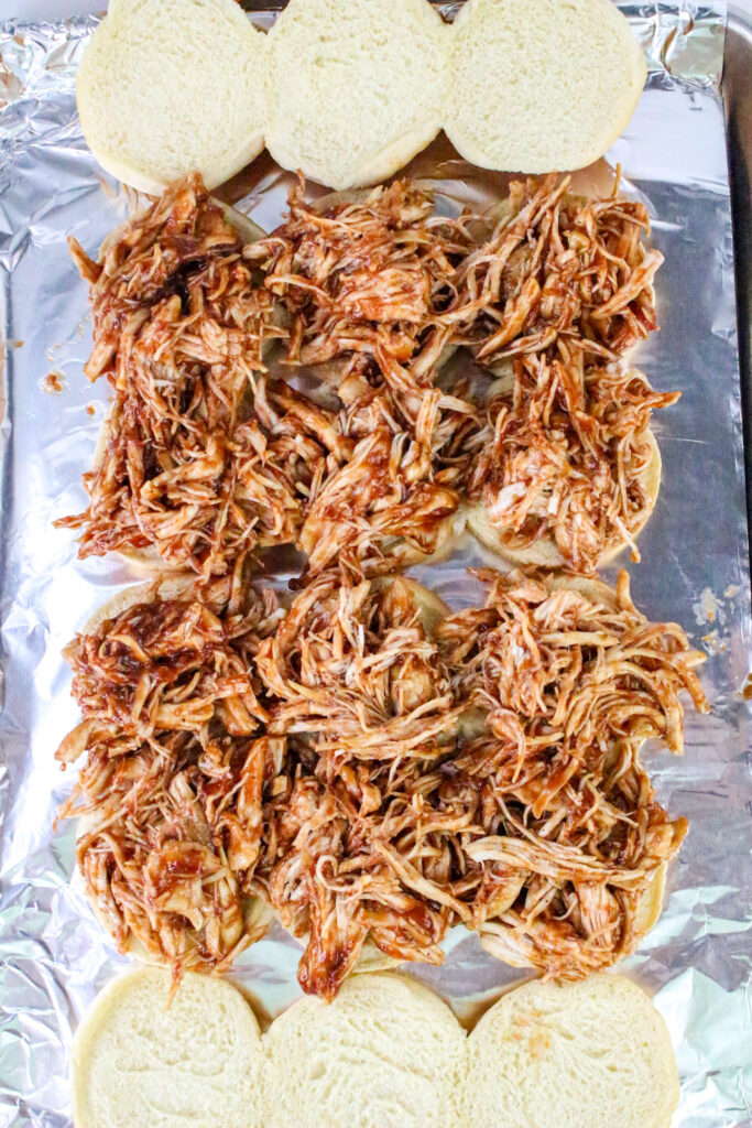 A picture of hawaiian rolls cut in half, topped with chicken seasoned with barbecue sauce.
