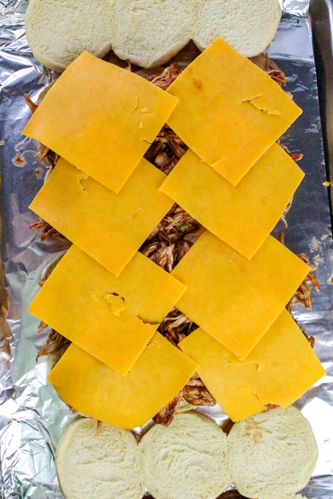 A picture of hawaiian rolls cut in half, topped with barbecue chicken and cheese.