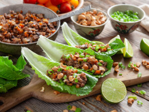 A picture of three chinese pork lettuce wraps surrounded by ingredients on a wooden serving platter.