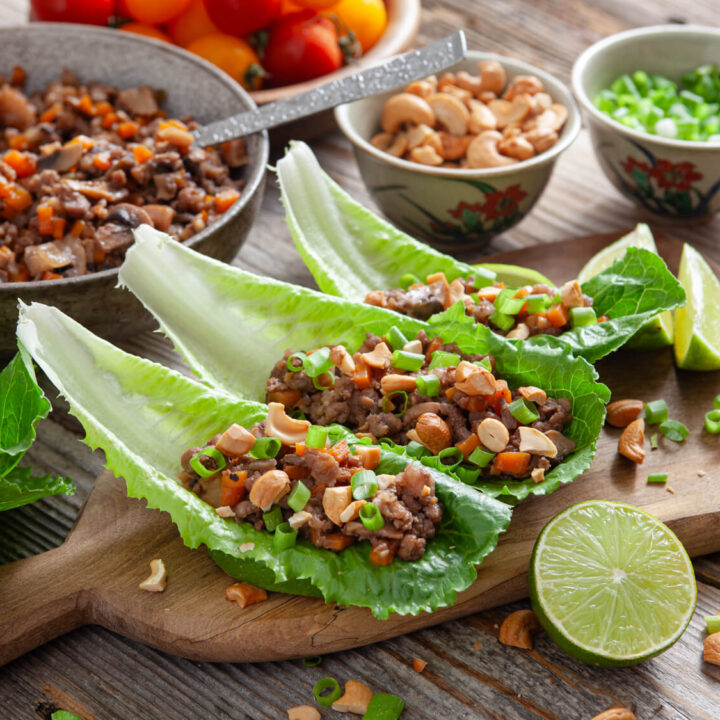 A picture of three chinese pork lettuce wraps surrounded by ingredients on a wooden serving platter.