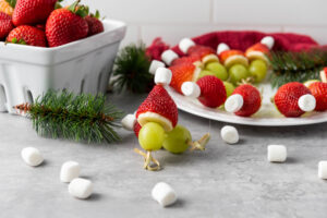 A picture of a Christmas themed fruit skewer with a plate of fruit skewers in the background.