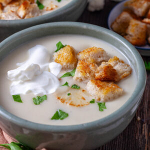 A picture of cauliflower soup in a bowl with sour cream and croutons.