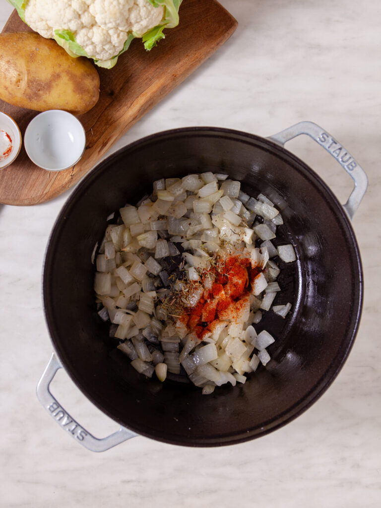 A picture of onions and garlic cooking with thyme and paprika in a pot.