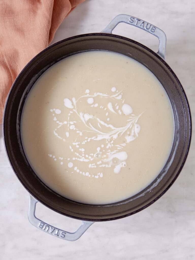 A picture of finished cauliflower soup in a pot. with a drizzle finish of sour cream.