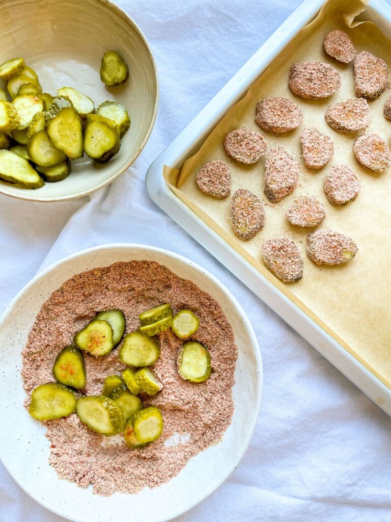 A picture of sliced, breaded pickles being arranged onto a baking sheet.