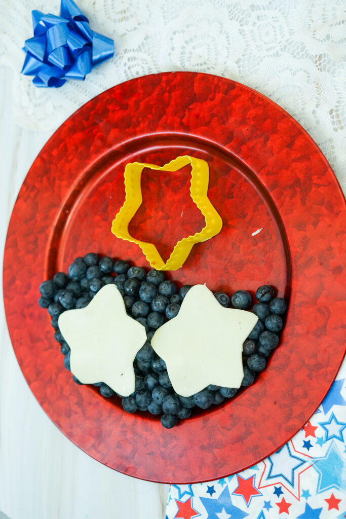 A picture of pieces of mozzarella cut into star shapes on top of a set of blueberries.