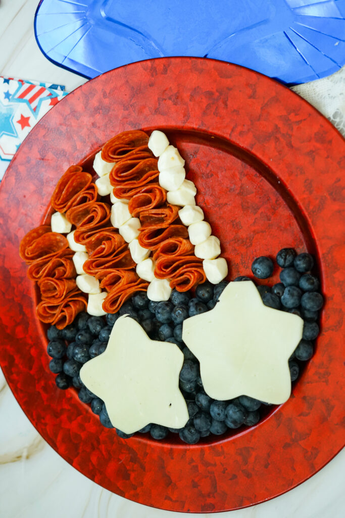A icture of blueberries, mozzarella, and pepperoni being arranged to appear like an American flag.