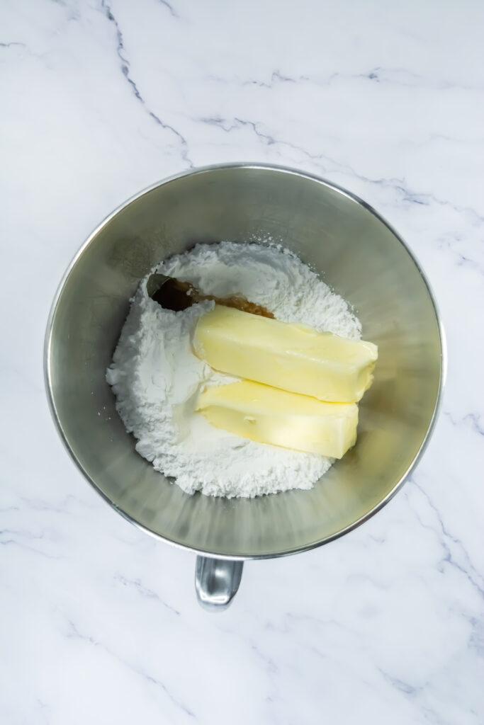 A picture of powdered sugar, softened butter, salt, and vanilla unmixed in a tin bowl.