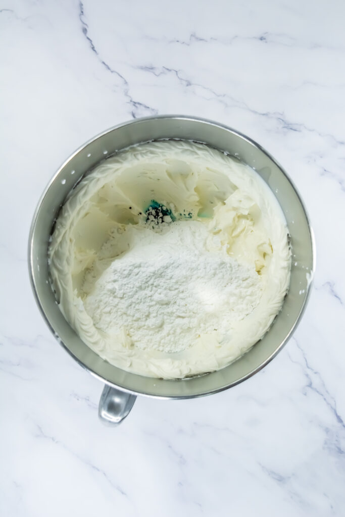 A picture of powdered sugar, milk and food coloring in a bowl with a butter sugar mixture.