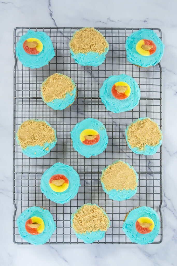 A picture of blue frosted cupcakes topped by Teddy Graham cookies and cookie crumbles.