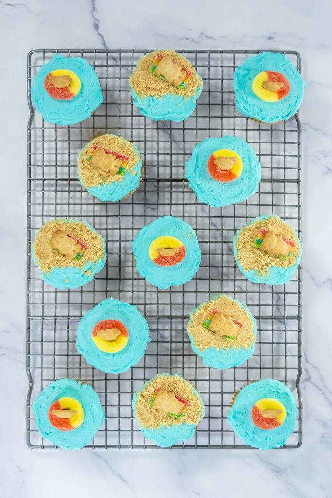 A picture of blue frosted cupcakes topped with candy and Teddy Graham cookies.