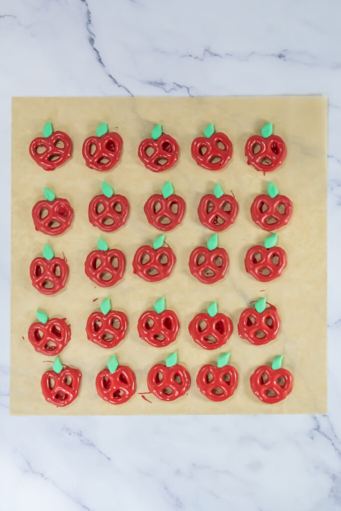 A picture of a large set of candy coated pretzels made to resemble apples topped with fondant leaves.