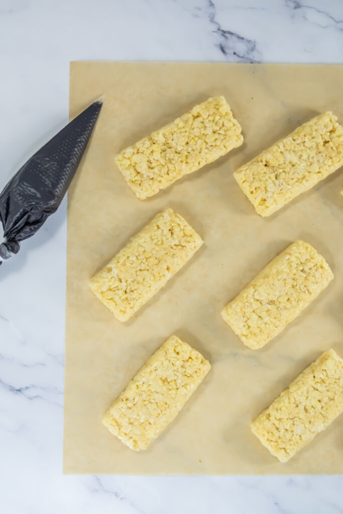A picture of rice krispy treats next to a piping bag filled with black candy frosting.