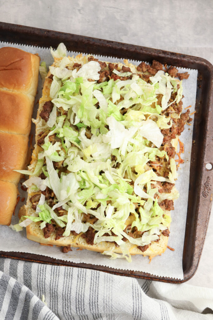 A picture of lettuce, ground beef, and melted cheese on Hawaiian rolls to make sliders.