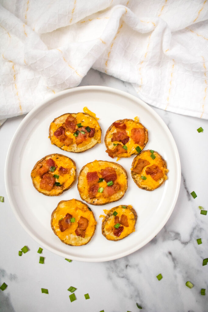 A picture of fully cooked bacon and cheese potato slices on a white plate.