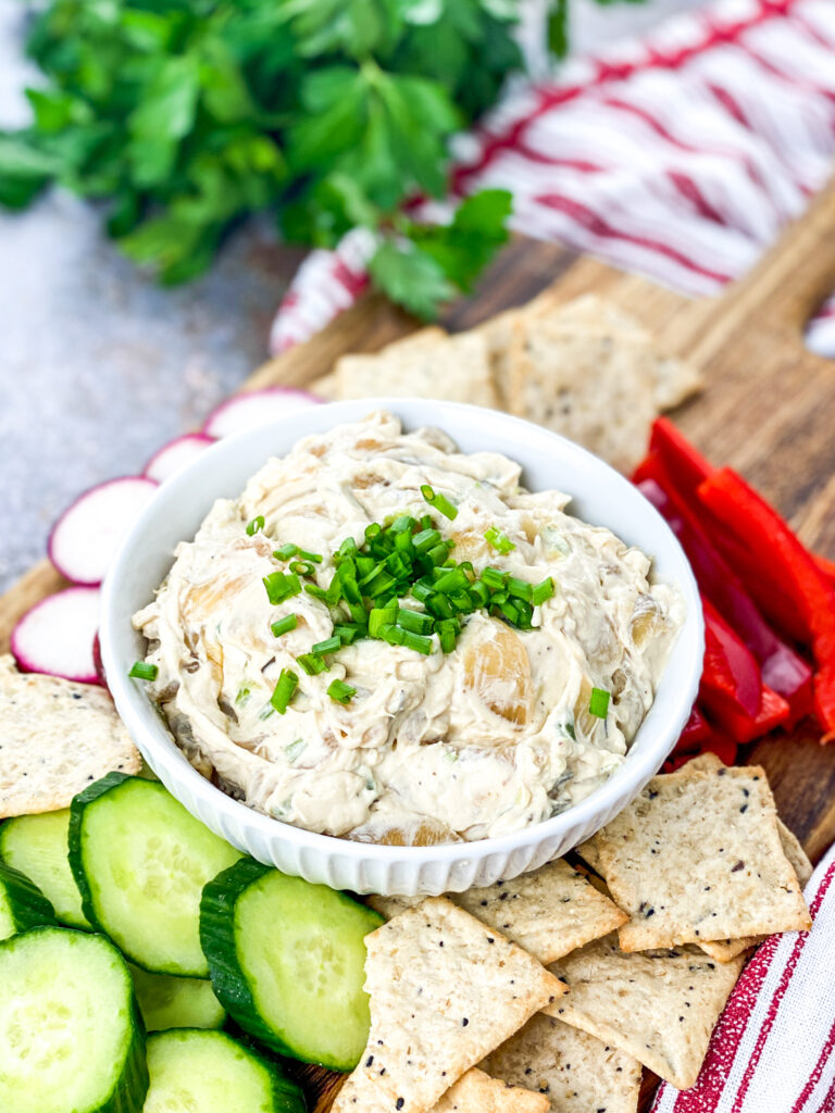 A picture of caramelized onion dip in a bowl with dippable vegetables and crackers around the bowl.