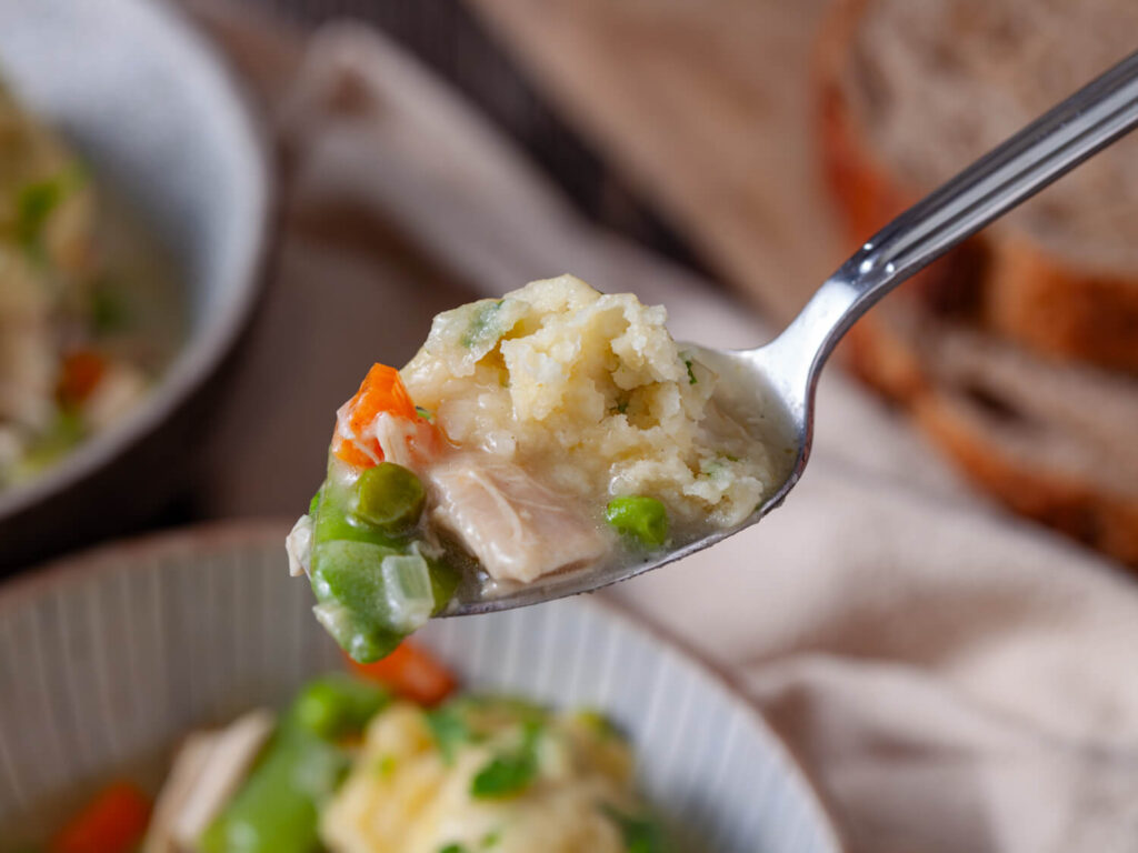 A picture of a spoonfull of chicken dumpling and soup with a bite taken out of the dumpling.