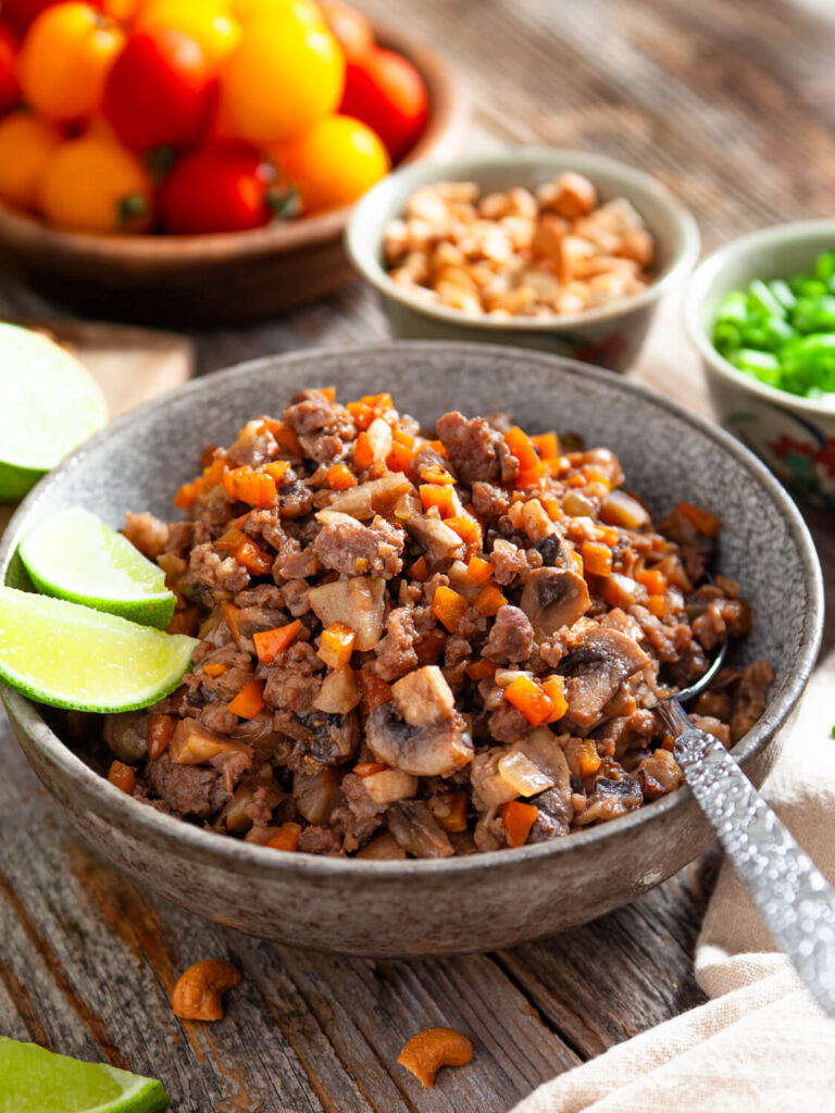 A picture of a large bowl of chinese pork garnished with lime wedges.