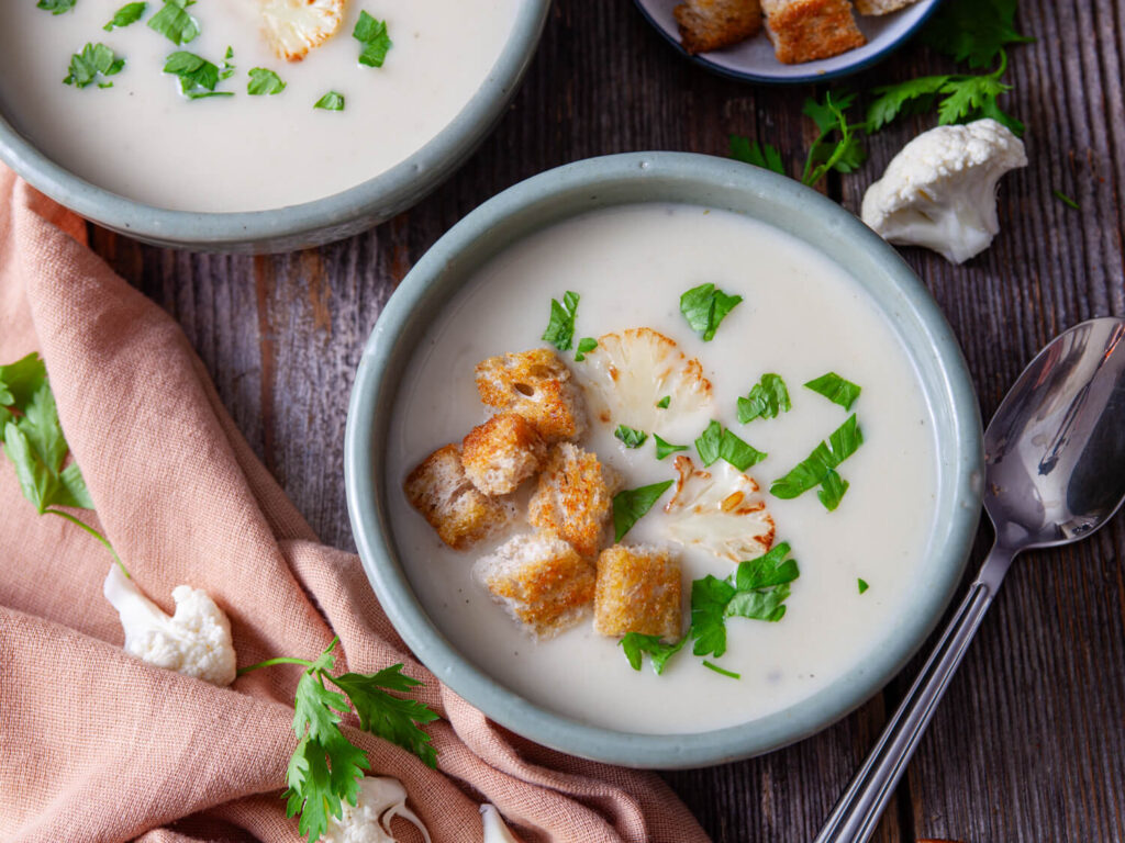 A top down picture of a bowl of cauliflower soup with croutons and herbs.