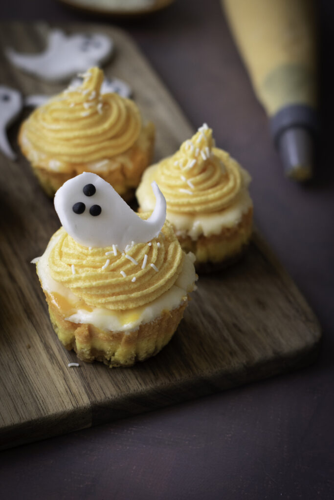 A picture of halloween mini cheesecakes with one topped by a sugar paste ghost.
