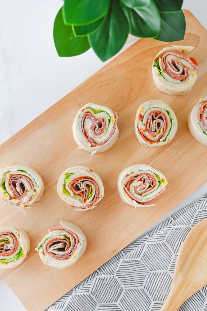 An overhead picture of rolled, sliced italian pinwheel sandwiches displayed on a wooden cutting board.