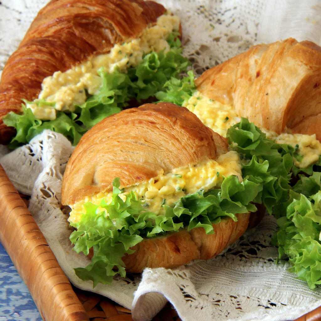 A close up picture of a pair of croissant egg salad sandwich.