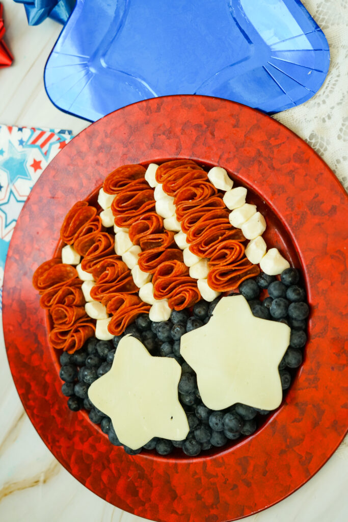 A icture of blueberries, mozzarella, and pepperoni being designed to appear like an American flag on a circular plate.