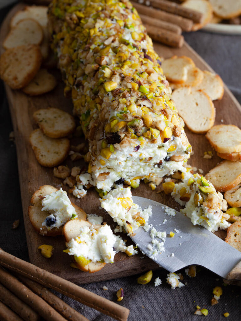 A picture of a pistachio and black currant cheese log with slices cut out of it.