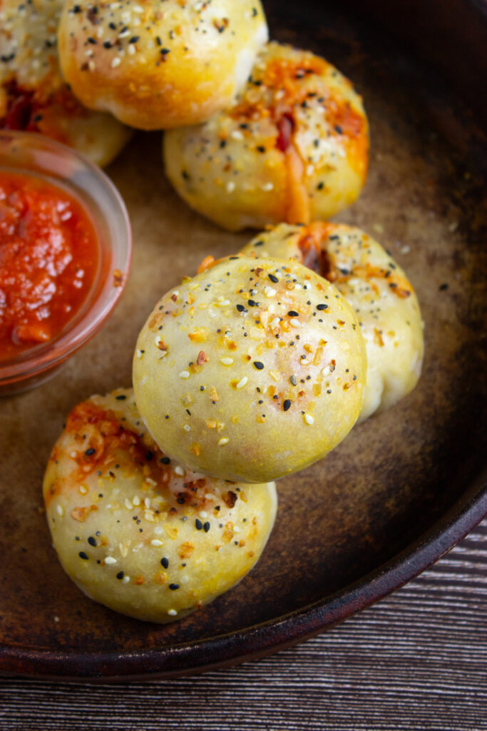 A picture of fully baked pizza bagel bites in a tin pan with more pizza sauce for dipping.