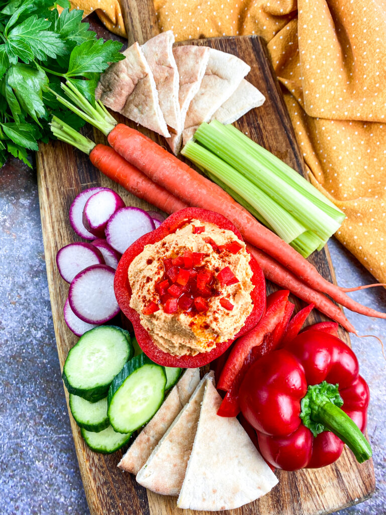 A picture of a red bell pepper stuffed with roasted hummus, arranged with various other vegetables.