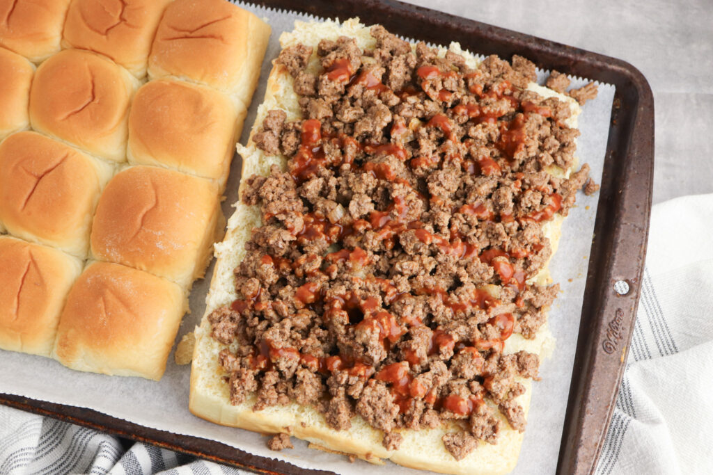 A picture of seasoned ground beef with taco sauce spread over Hawaiian rolls cut in half to make sandwiches.