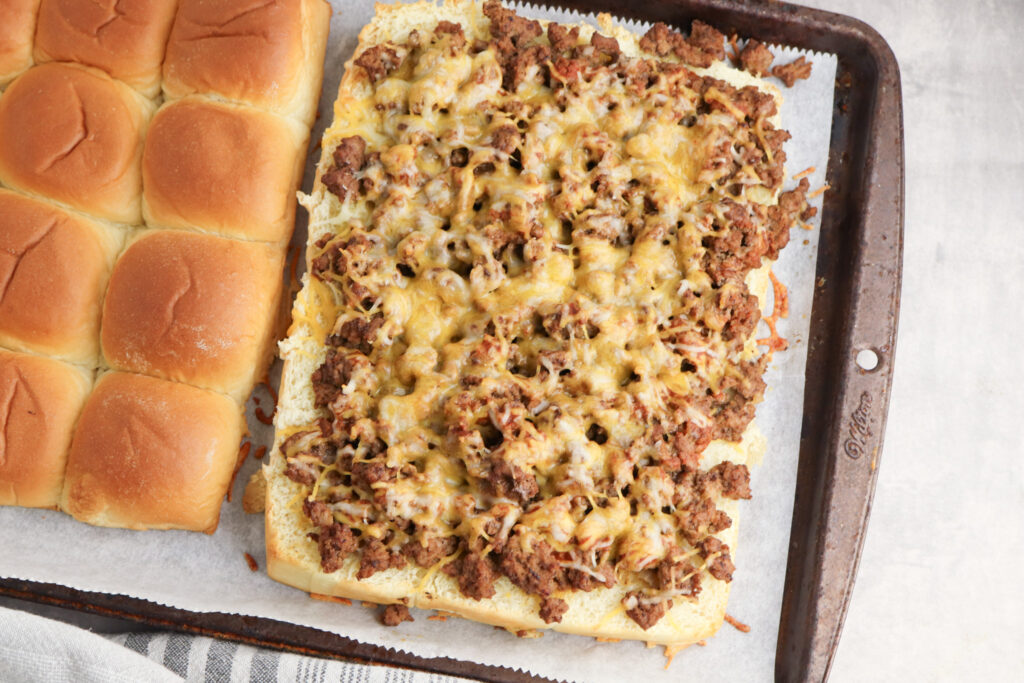 A picture of ground beef and melted cheese on Hawaiian rolls cut in half to make sandwiches.