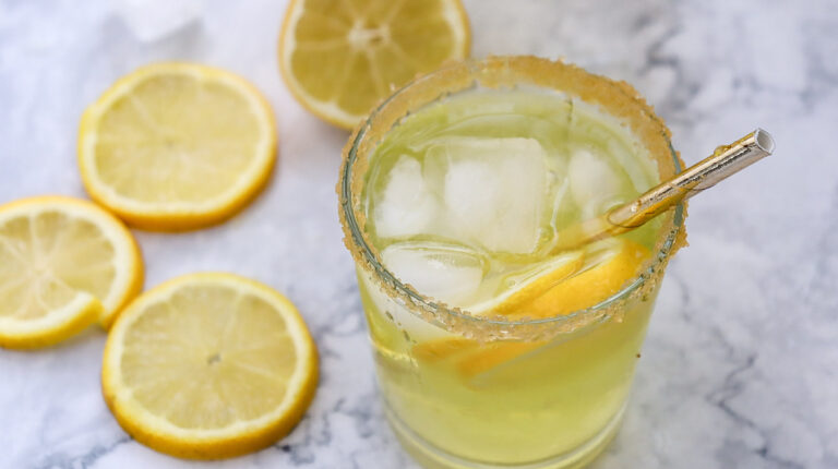 A glass of homemade lemonade flanked by three lemon slices.