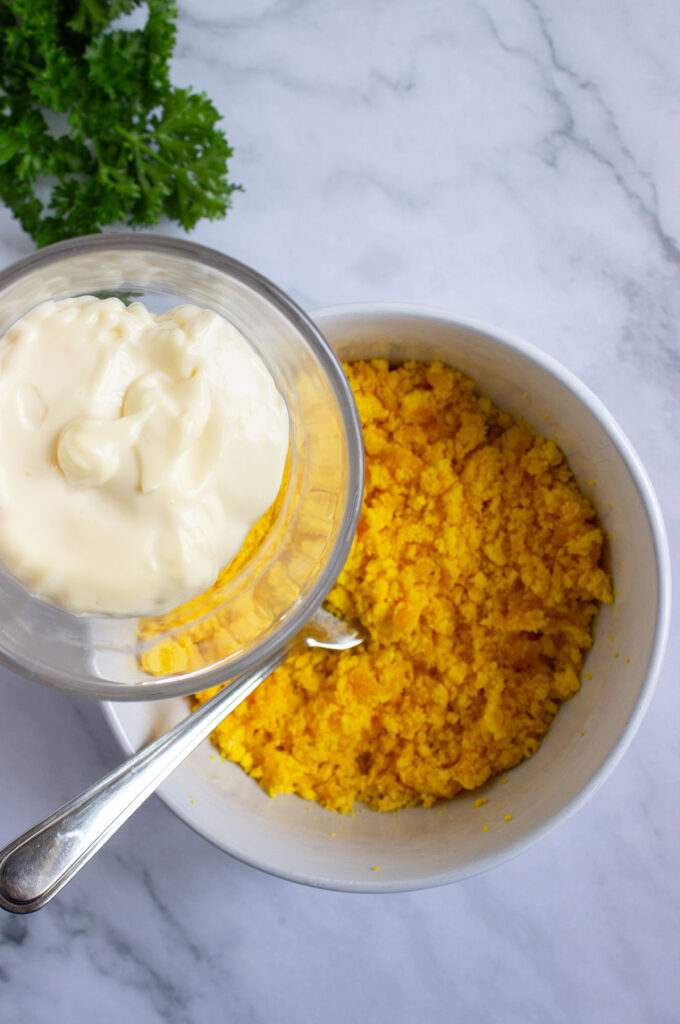 A picture of mayonnaise about to be poured into a bowl of crumbled hard boiled egg yolks.
