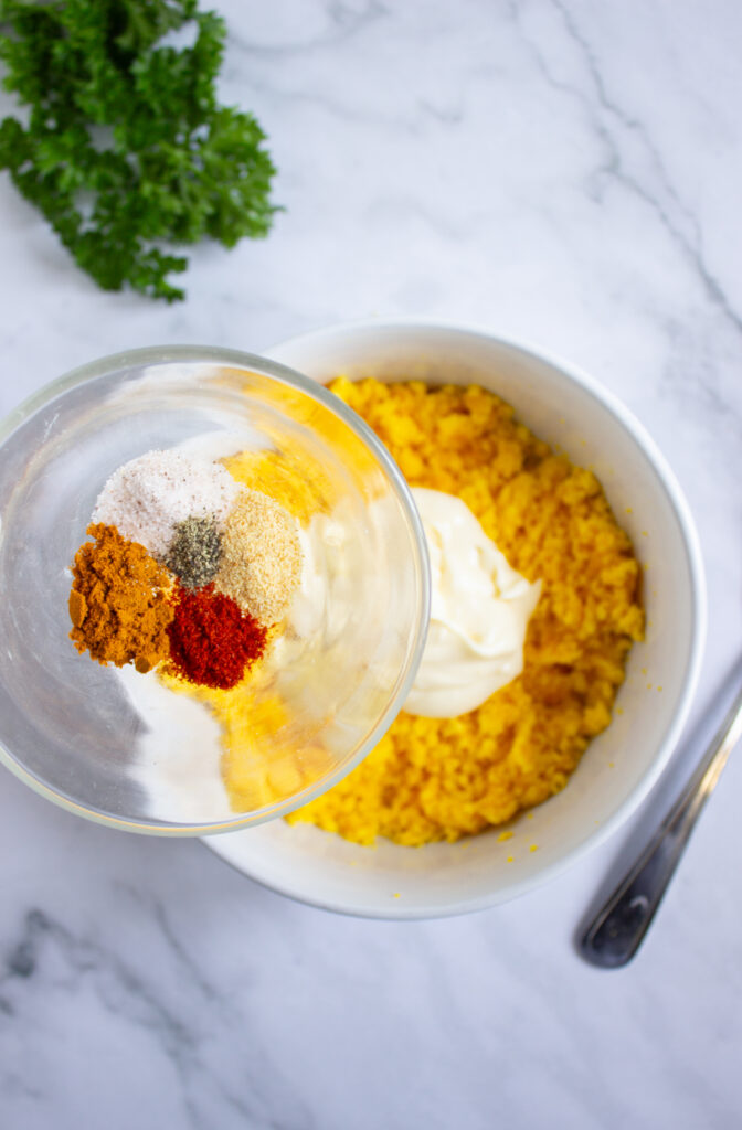 A picture of spices about to be poured into a bowl of mayonnaise, dijon mustard, and crumbled hard boiled egg yolks.