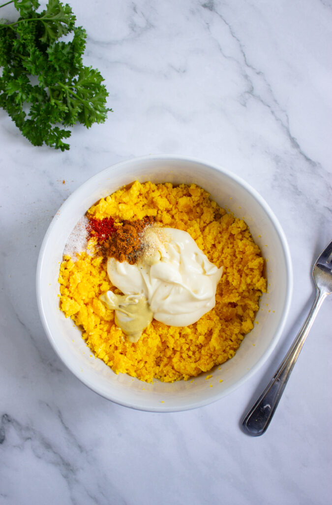 A picture of spices, mayonnaise, dijon mustard, and crumbled hard boiled egg yolks unmixed together in a bowl.