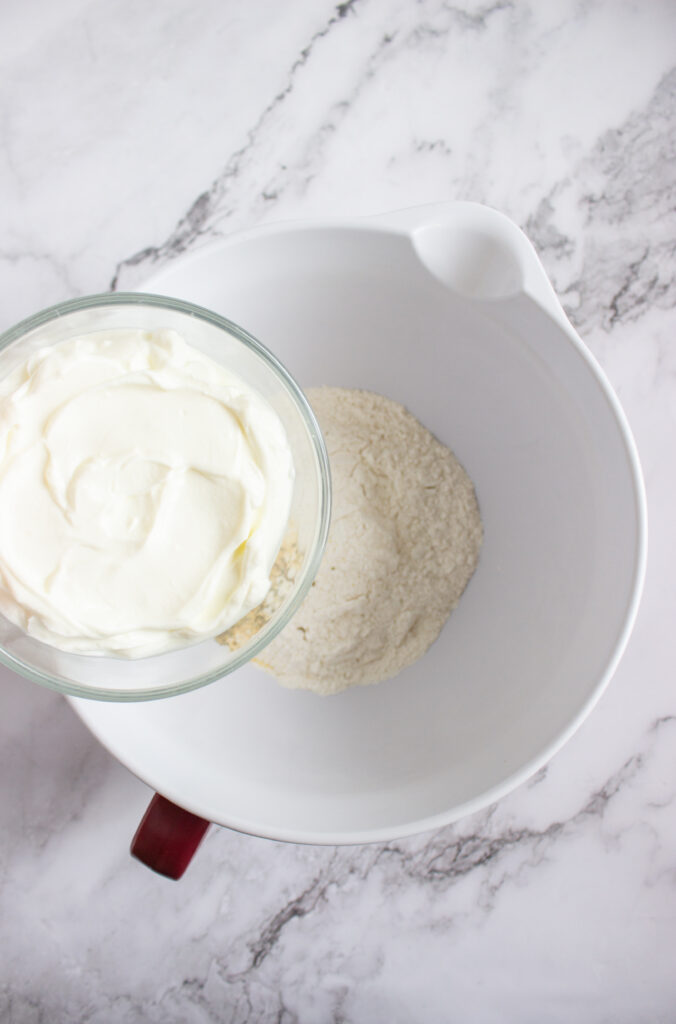 A picture of greek yogurt being aded to a bowl of flour and spices.