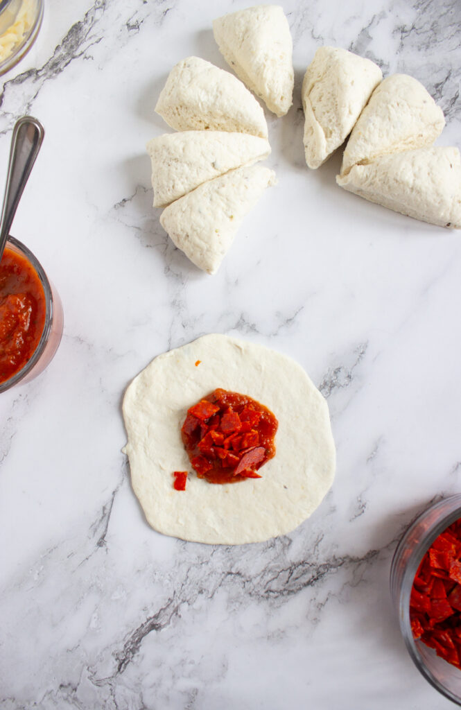 A picture of flattened bagel dough topped with pizza sauce and pepperoni.