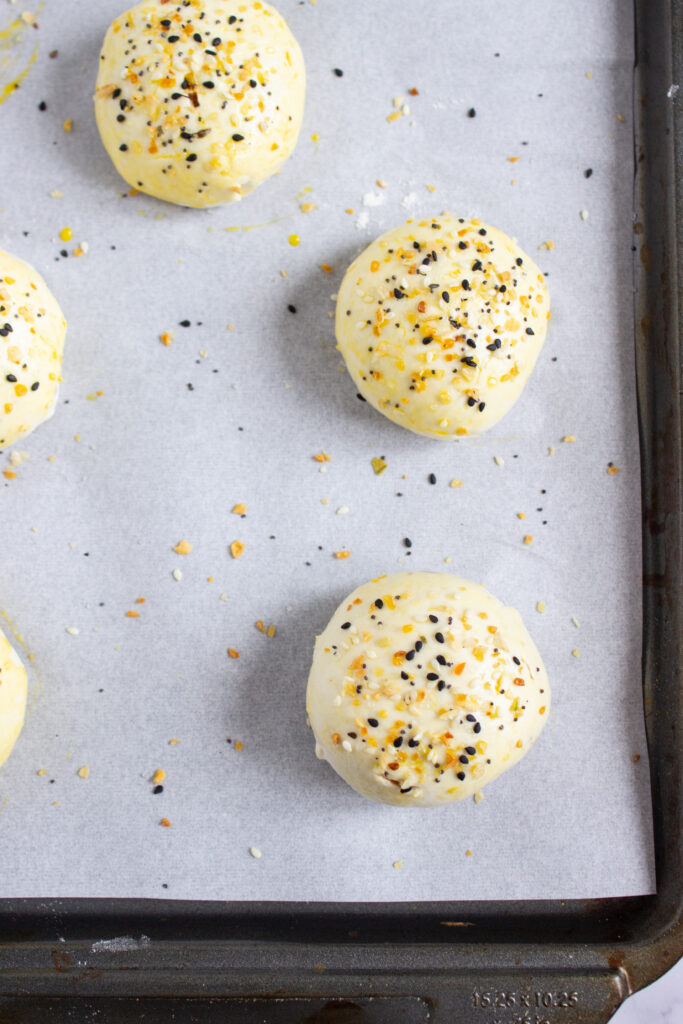 A picture of balls of bagel dough sprinkled with erveything bagel seasoning.