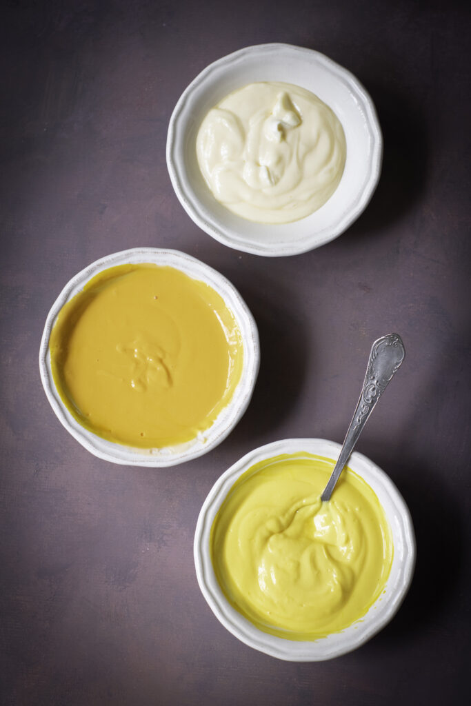 A picture of white, orange, and yellow bowls of cheesecake batter.