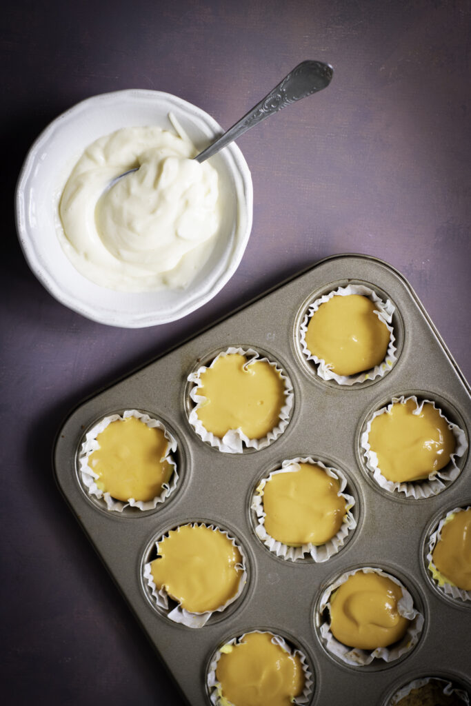 A picture of orange cheesecake batter topping yellow cheesecake batter in cupcake tins.