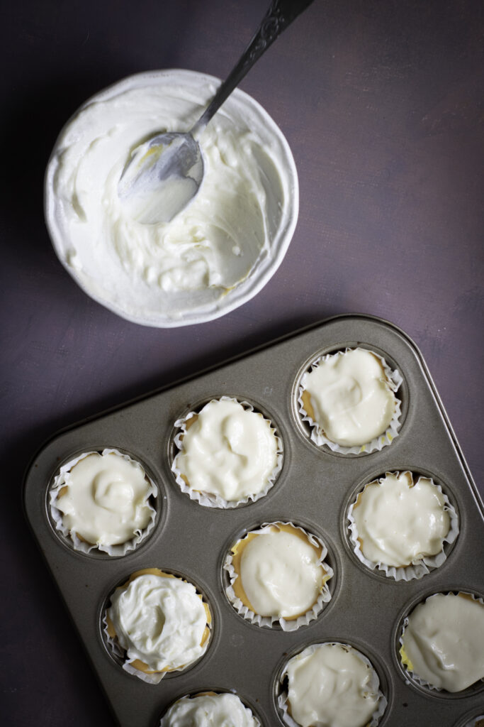 A picture of white cheesecake batter topping yellow and orange cheesecake batter in cupcake tins.
