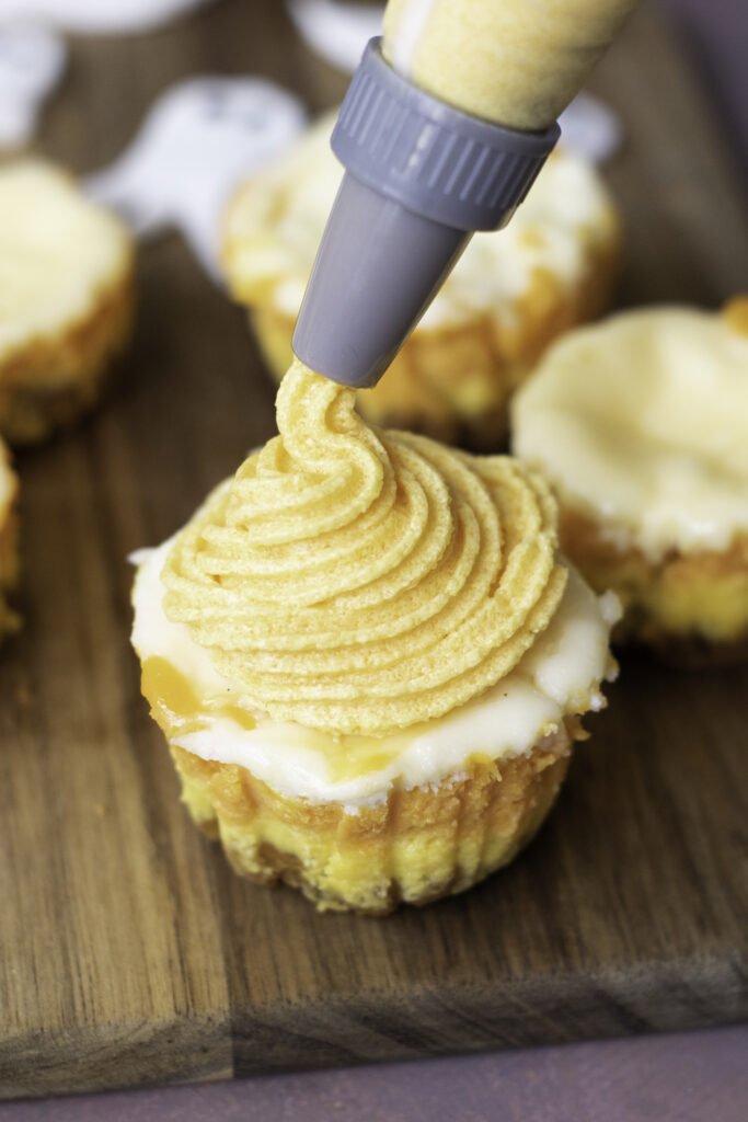 A picture of a halloween mini cheesecake being decorated with orange frosting.
