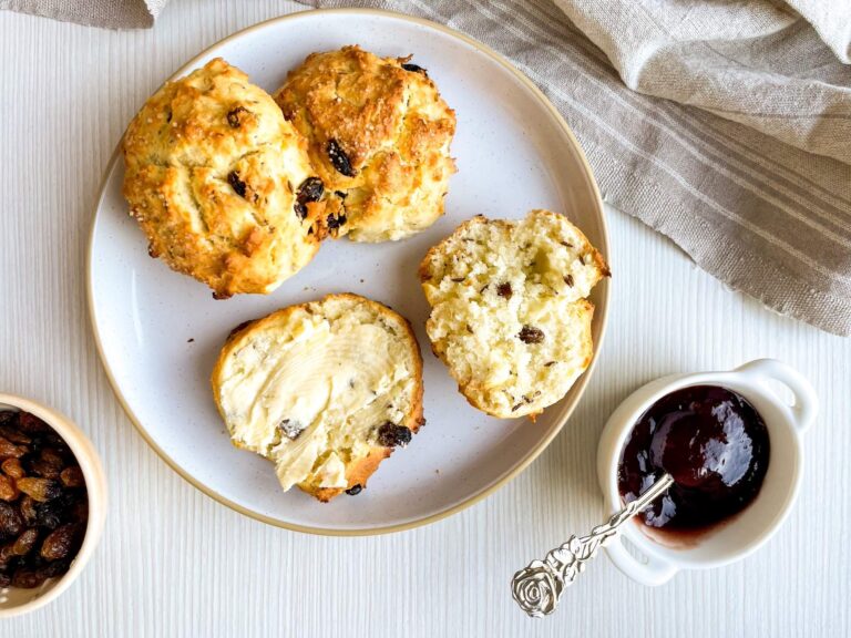 A picture of irish soda scones with one cut in half and a container of jam on the side.